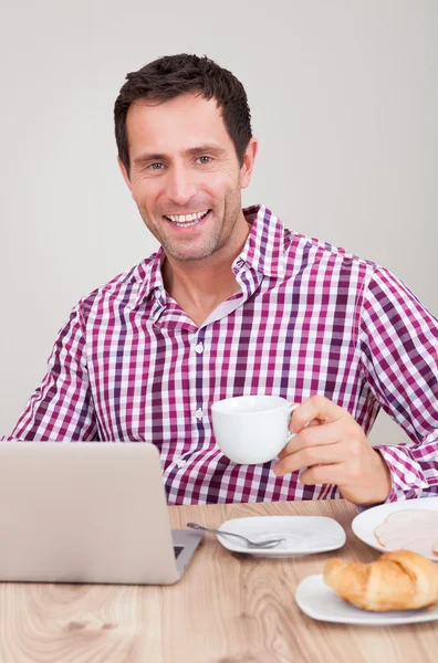 在吃早饭时使用便携式计算机的年轻男子的画像 — 图库照片