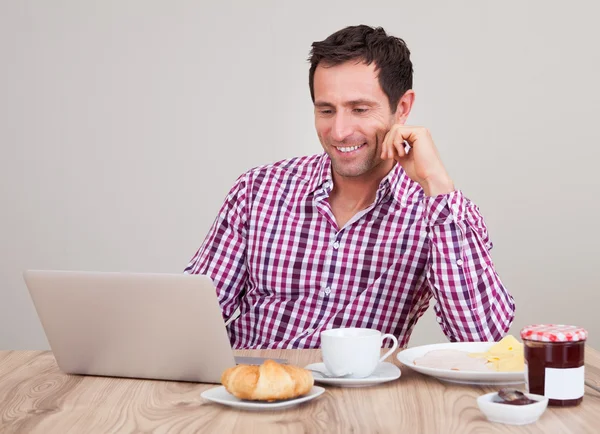 Portret van een jonge man met behulp van laptop bij het ontbijt — Stockfoto