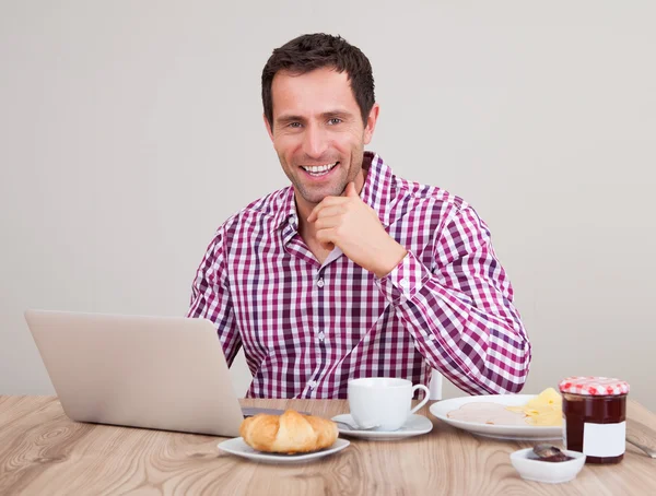 Retrato de hombre joven usando el ordenador portátil en el desayuno — Foto de Stock