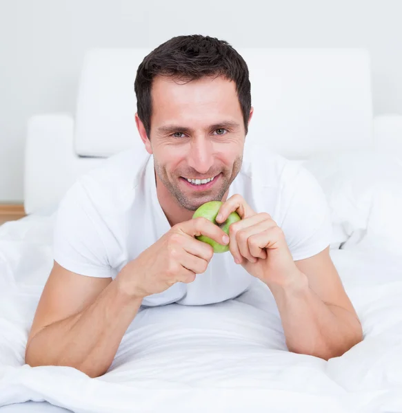 Молодий чоловік лежить на ліжку тримає зелене яблуко — стокове фото