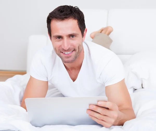 Retrato de un joven acostado en la cama usando un ordenador portátil — Foto de Stock