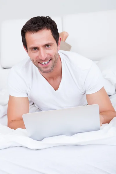 Portret młodego człowieka leżącego na łóżku za pomocą laptopa — Zdjęcie stockowe