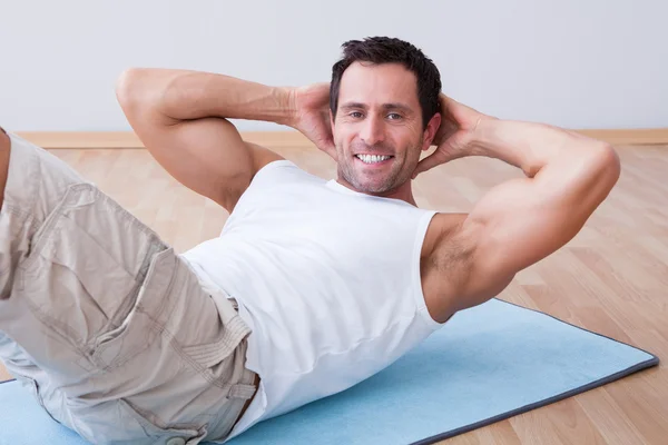 Hombre joven haciendo ejercicio en la esterilla de ejercicio — Foto de Stock