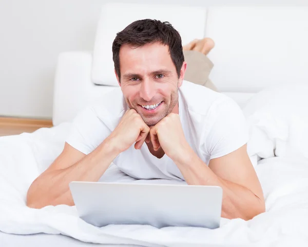 Retrato de un joven acostado en la cama usando un ordenador portátil — Foto de Stock