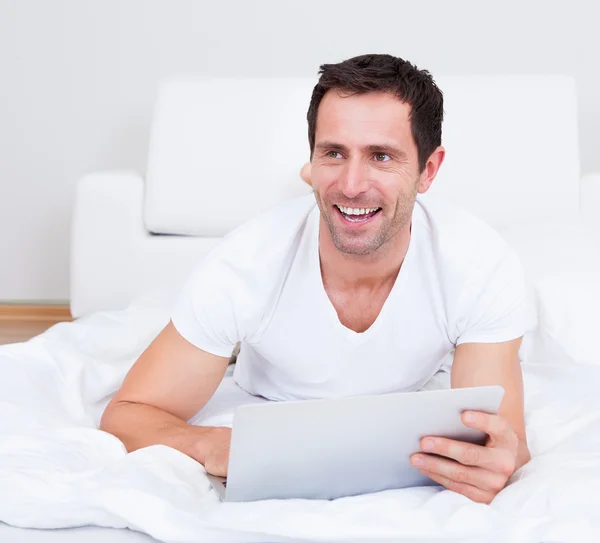 Porträt eines jungen Mannes, der mit Laptop auf dem Bett liegt — Stockfoto