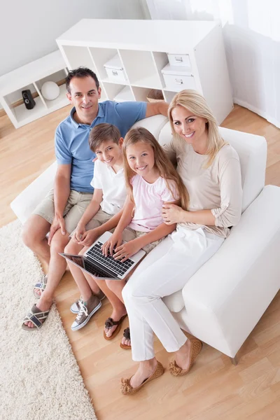 Familia feliz sentada en un sofá usando un ordenador portátil — Foto de Stock