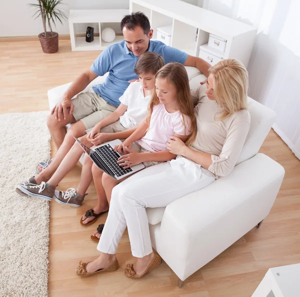 Glückliche Familie sitzt auf einem Sofa mit Laptop — Stockfoto