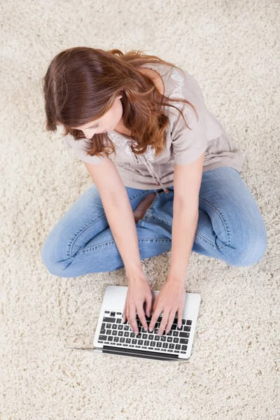 Jonge vrouwelijke zittend op het tapijt met behulp van een laptop — Stockfoto