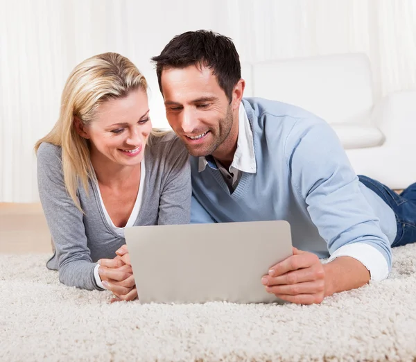 Casal deitado em um tapete com um laptop — Fotografia de Stock