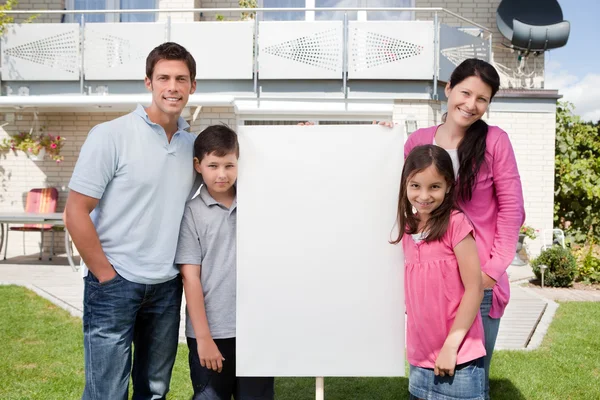 Pequeña familia parada afuera con un cartel vacío — Foto de Stock