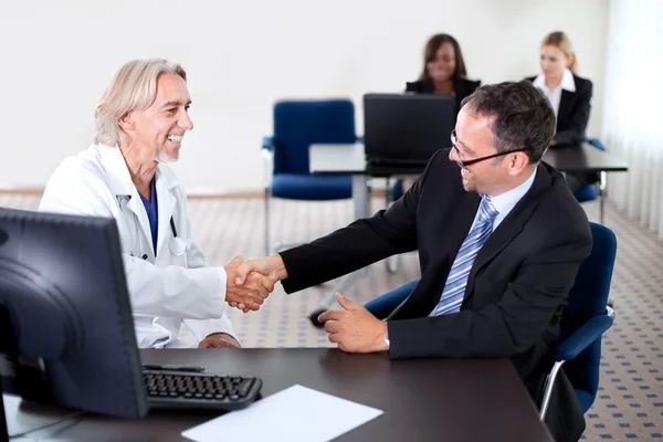 Doctor estrechando la mano con un paciente en un escritorio — Foto de Stock