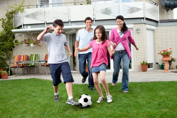 Famille heureuse jouant au football dans leur jardin — Photo