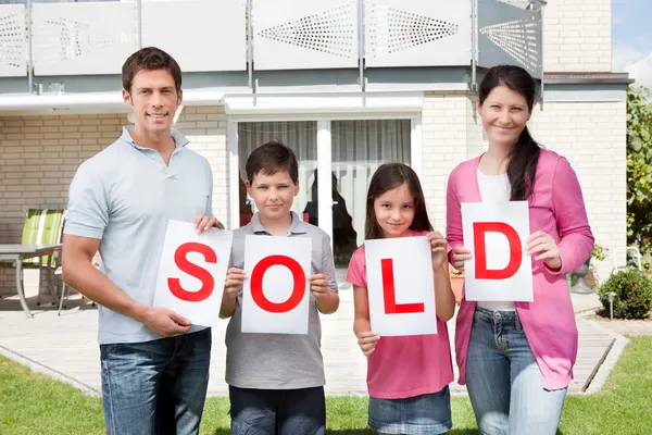 Familia sosteniendo un cartel vendido fuera de su casa — Foto de Stock