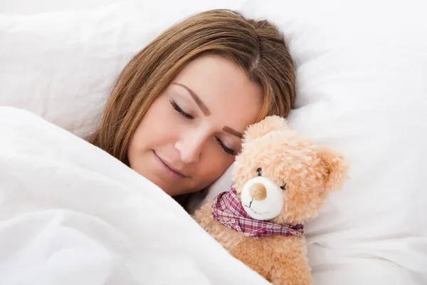 Onun oyuncak ayı ile yatakta uyuyan genç güzel kadın — Stok fotoğraf