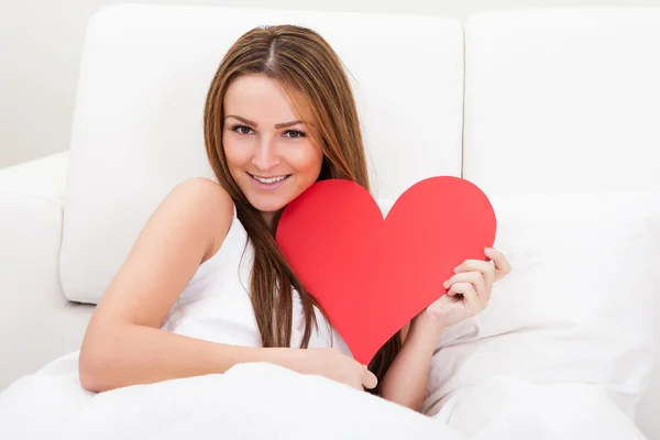 Young Beautiful Woman Lying On Bed And Holding Heart Shape — Stock Photo, Image