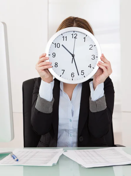 Geschäftsfrau hält Uhr im Büro vor dem Gesicht — Stockfoto