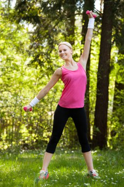 Dambıllarla egzersiz yapan genç bir kadın.