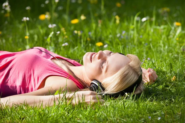 Kvinna liggande på gräs lyssnar musik — Stockfoto