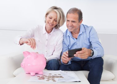 Mature Couple Calculating Coin In The Piggybank clipart
