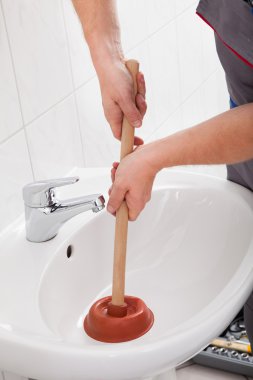 Plumber using plunger in sink clipart