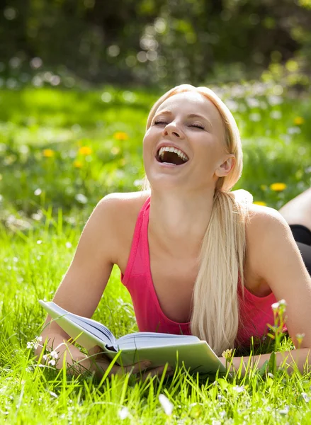 Schöne Frau liegt lachend im Gras und liest Buch — Stockfoto