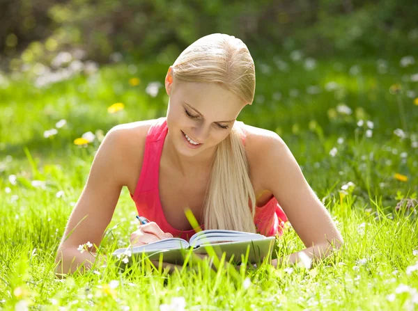 Junge schöne Frau liegt im Gras und schreibt Tagebuch — Stockfoto