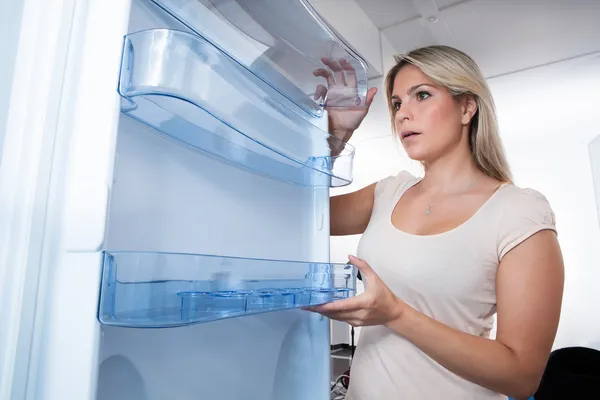 Junge Frau schaut in leeren Kühlschrank — Stockfoto