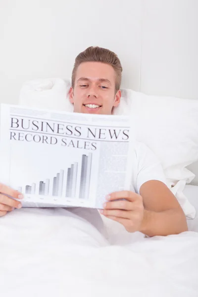 Fiatal férfi feküdt ágyban olvasó újság — Stock Fotó