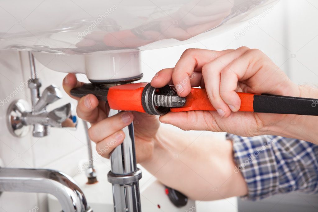 Young plumber fixing a sink in bathroom