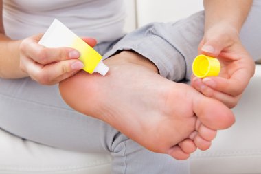 Woman applying cream on feet clipart