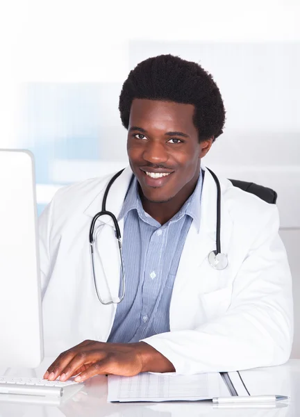 Docteur heureux avec stéthoscope assis à un bureau — Photo