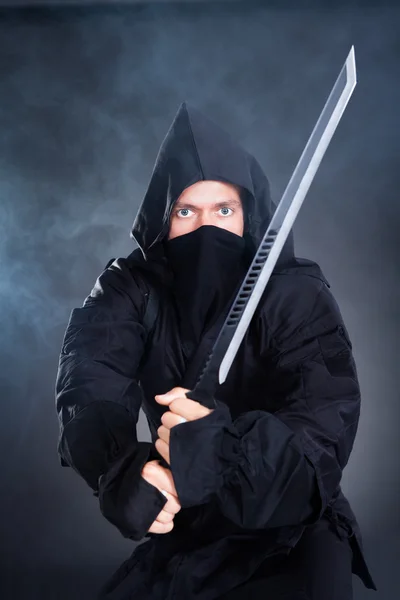 Мужчина-ниндзя в чёрном костюме с мечом в руках — стоковое фото