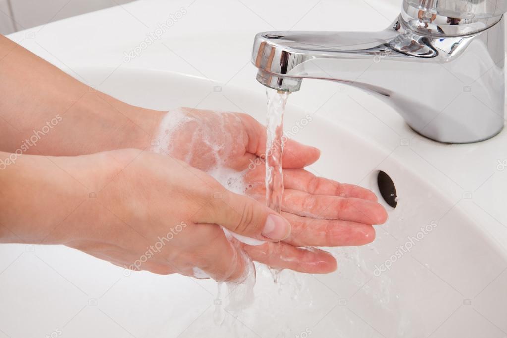 Human hands being washed under faucet