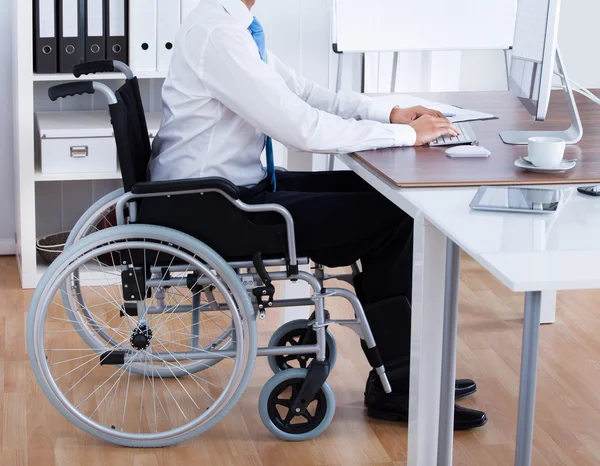 Бизнесмен, сидящий на инвалидной коляске и использующий компьютер — стоковое фото