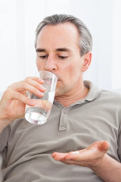 Ill man taking medication sitting up holding a glass of water — Stock Photo, Image