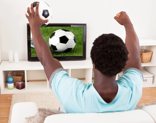 African Young Man Watching Television Holding Football — Stock Photo, Image
