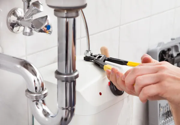 Young plumber fixing a sink in bathroom — Stock Photo, Image