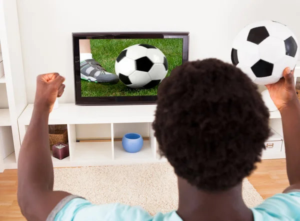 Νεαρός αφρικανική βλέποντας τηλεόραση εκμετάλλευσης της ποδοσφαίρου — Φωτογραφία Αρχείου
