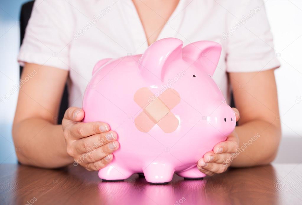 Young Businesswoman Holding Piggybank With Band Aid