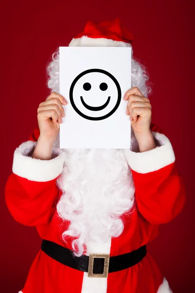Santa segurando sorridente na frente de seu rosto — Fotografia de Stock