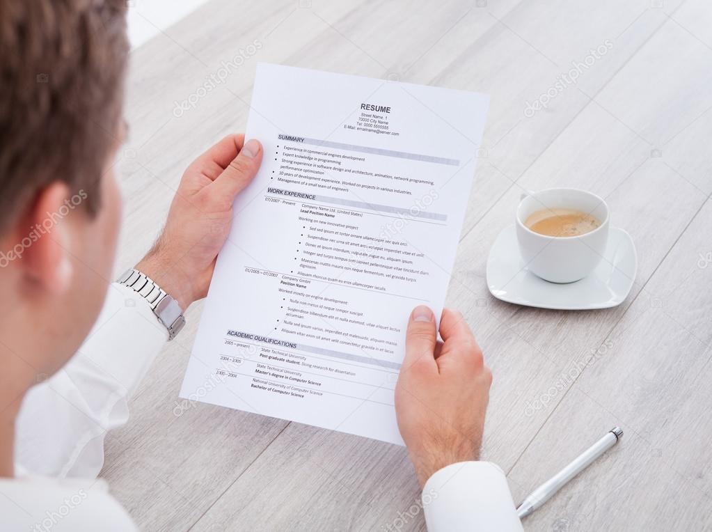 Businessman Reading Resume With Tea Cup On Desk