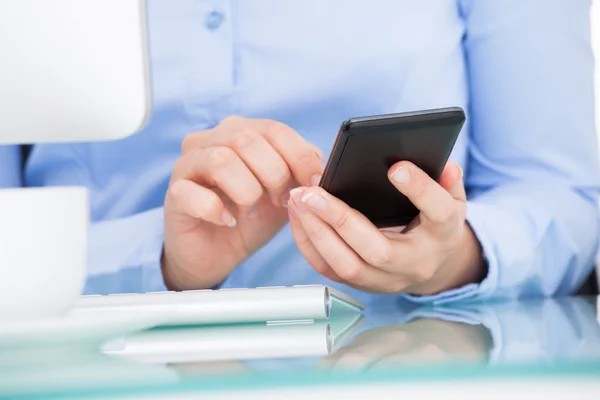 Empresária usando celular sentado na frente do computador — Fotografia de Stock