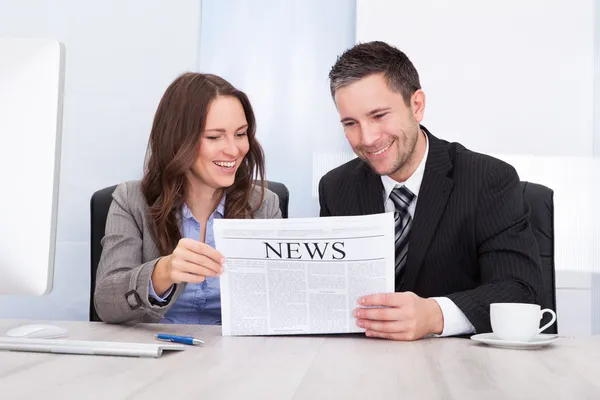 Счастливые бизнесмены читают газеты за рабочим столом — стоковое фото