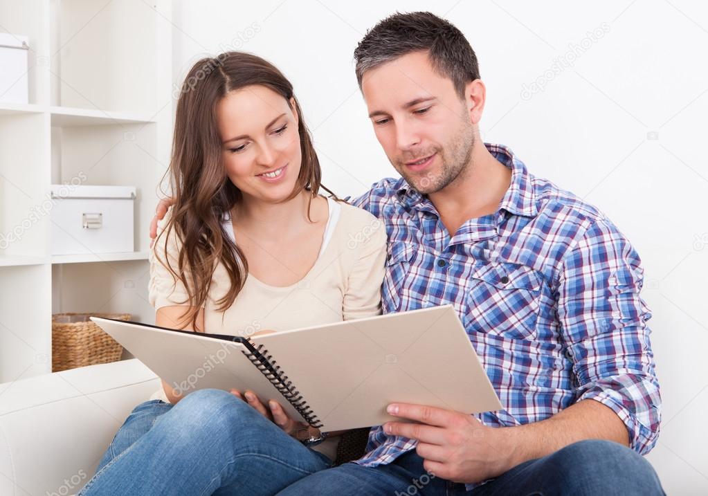 Couple Sitting On Couch Looking At Photo Album