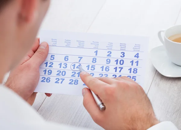 Homem marcando com caneta e olhando para data no calendário — Fotografia de Stock