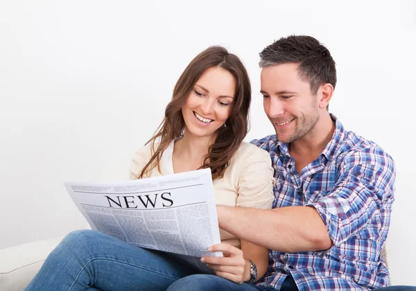 Felice giovane coppia seduta sul divano lettura giornale — Foto Stock