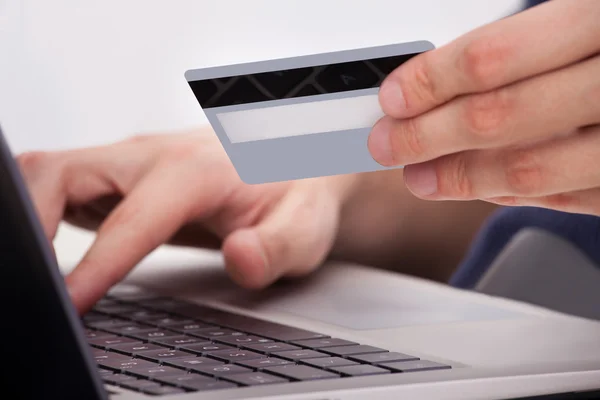 Persona que sostiene la tarjeta de crédito usando el ordenador portátil — Foto de Stock