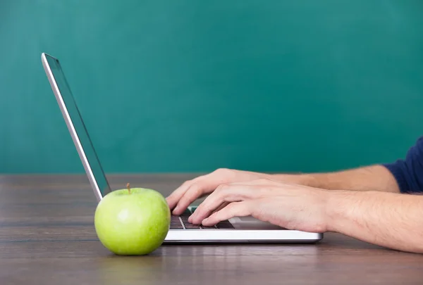 Persona che utilizza il computer portatile oltre alla mela verde — Foto Stock