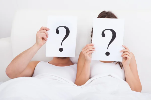 Casal deitado na cama segurando o ponto de interrogação — Fotografia de Stock