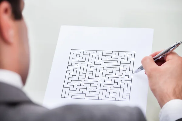 Empresário olhando para labirinto Puzzle segurando caneta — Fotografia de Stock